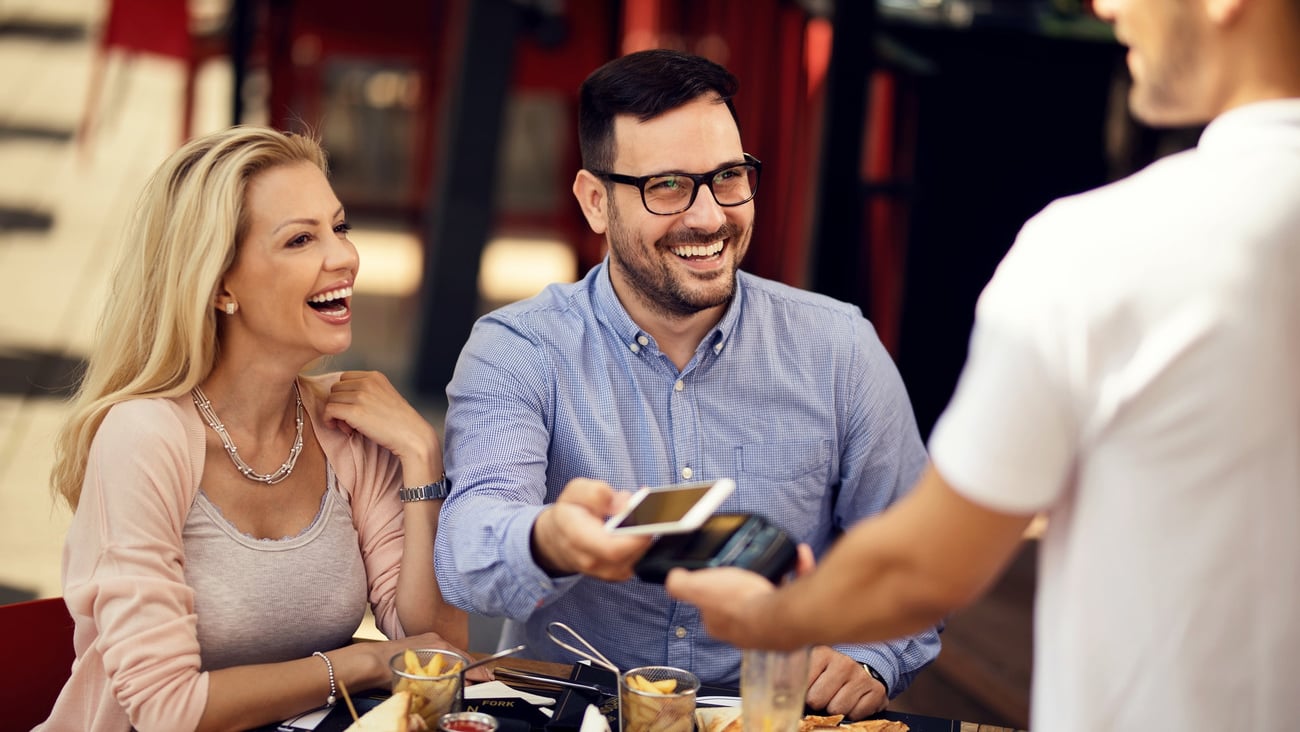 Happy couple having fun while making contactless payment via smart phone in a bar. ; Shutterstock ID 1465891616