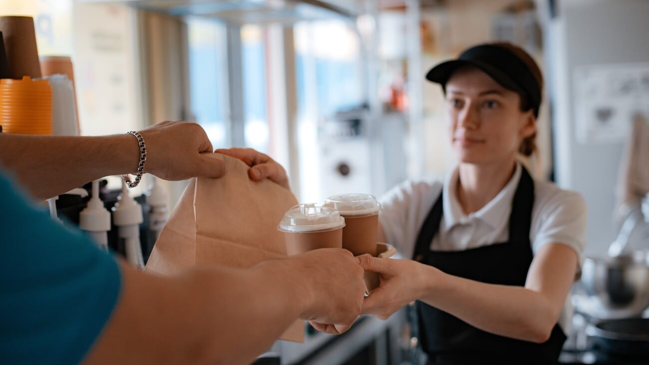 Buying fast food. A pancake with filling and a paper cup with coffee in the hands of a woman seller and a customer in the cafeteria. Takeaway food.; Shutterstock ID 2261755899
