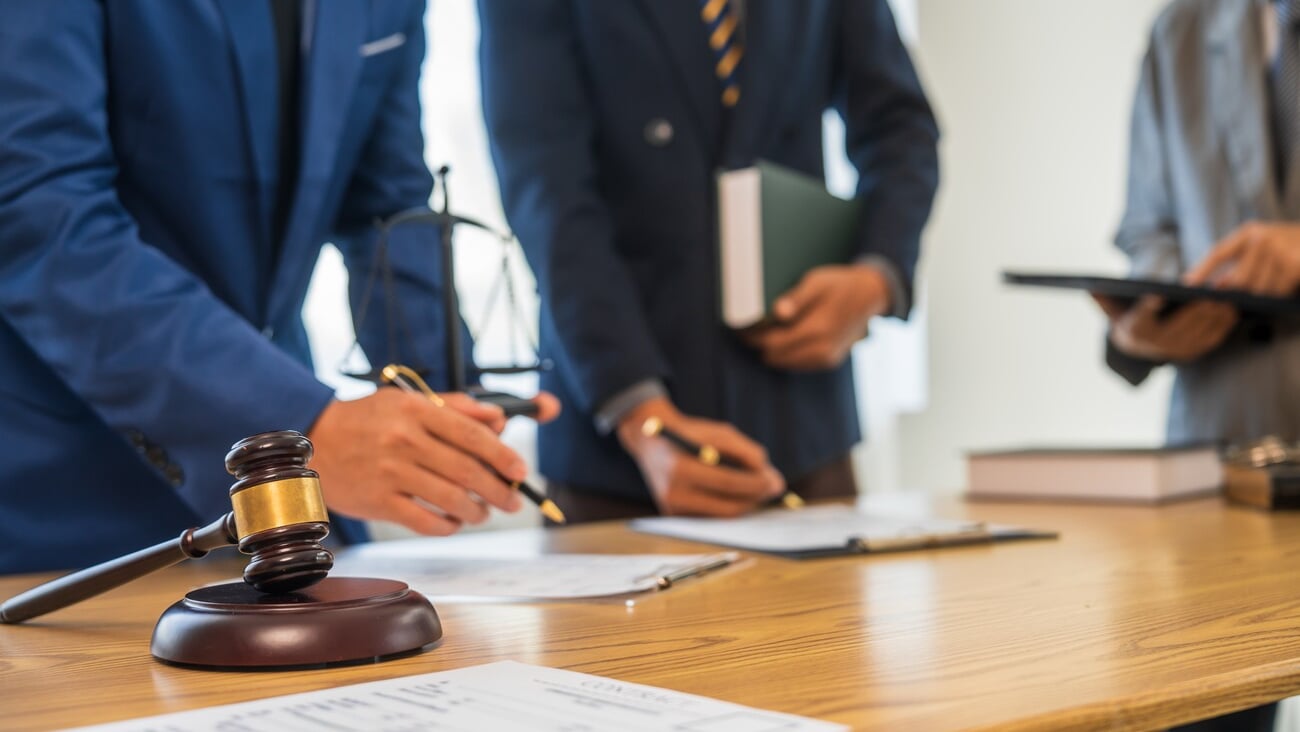 A team meeting of business people and a lawyer in formal suits is taking place at a desk, discussing a contract and various aspects of the law and litigation.; Shutterstock ID 2469307669