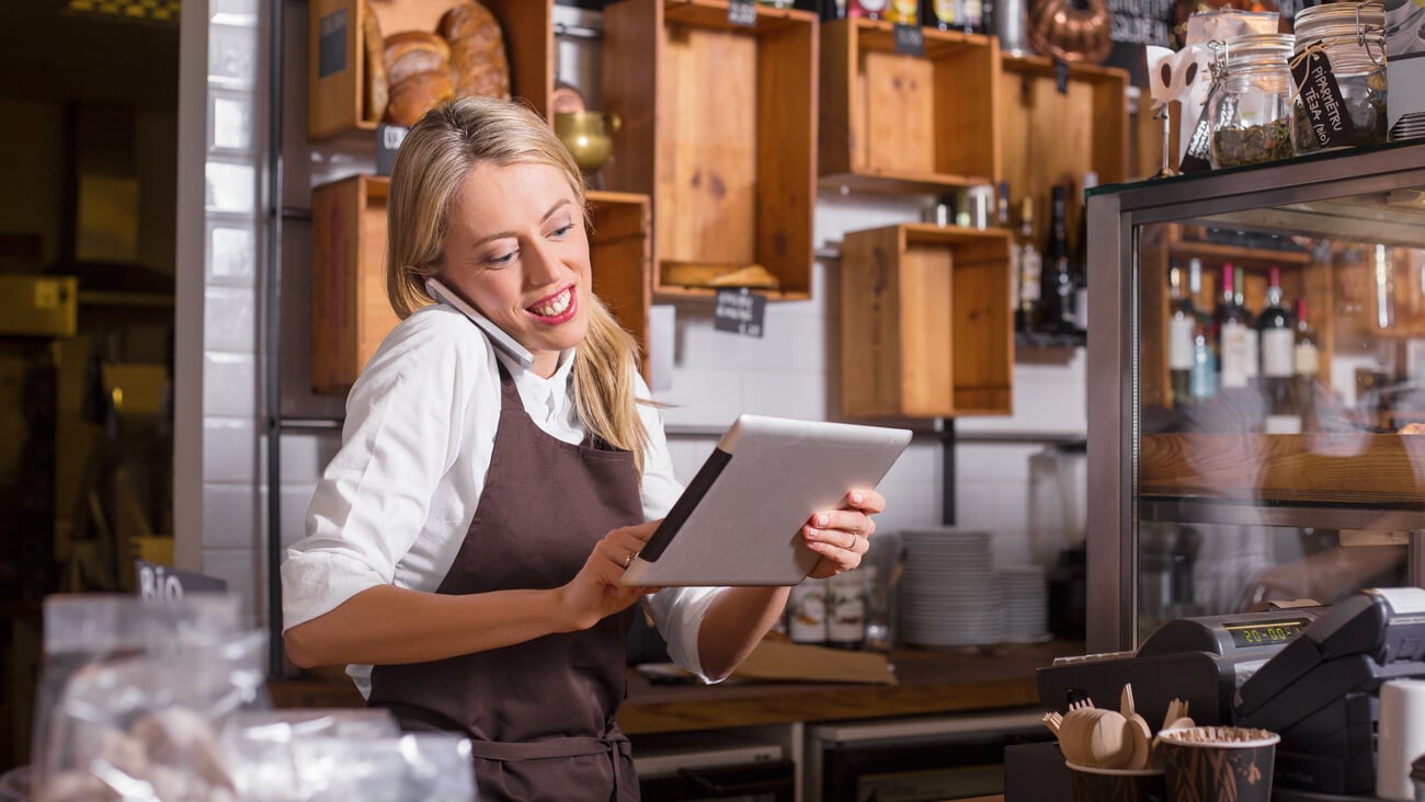 Female barista talking on the phone and using tablet while standing behind the counter; Shutterstock ID 422291380