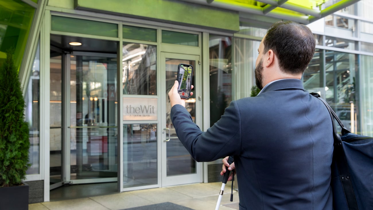 Man using the Be My Eyes app at a Hilton front entrance