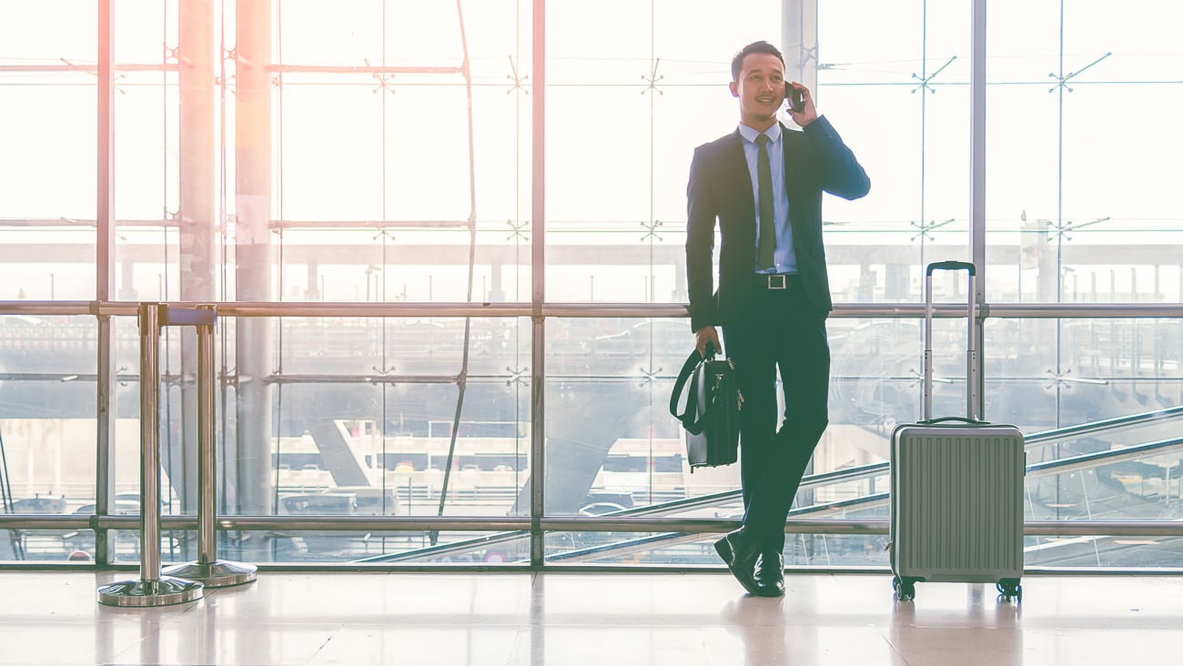 Businessman with a baggage talking via mobile phone at the airport. Businessman wearing suit jacket indoors. A man standing with a baggage using a smart phone in airport departure terminal. ; Shutterstock ID 1029773356