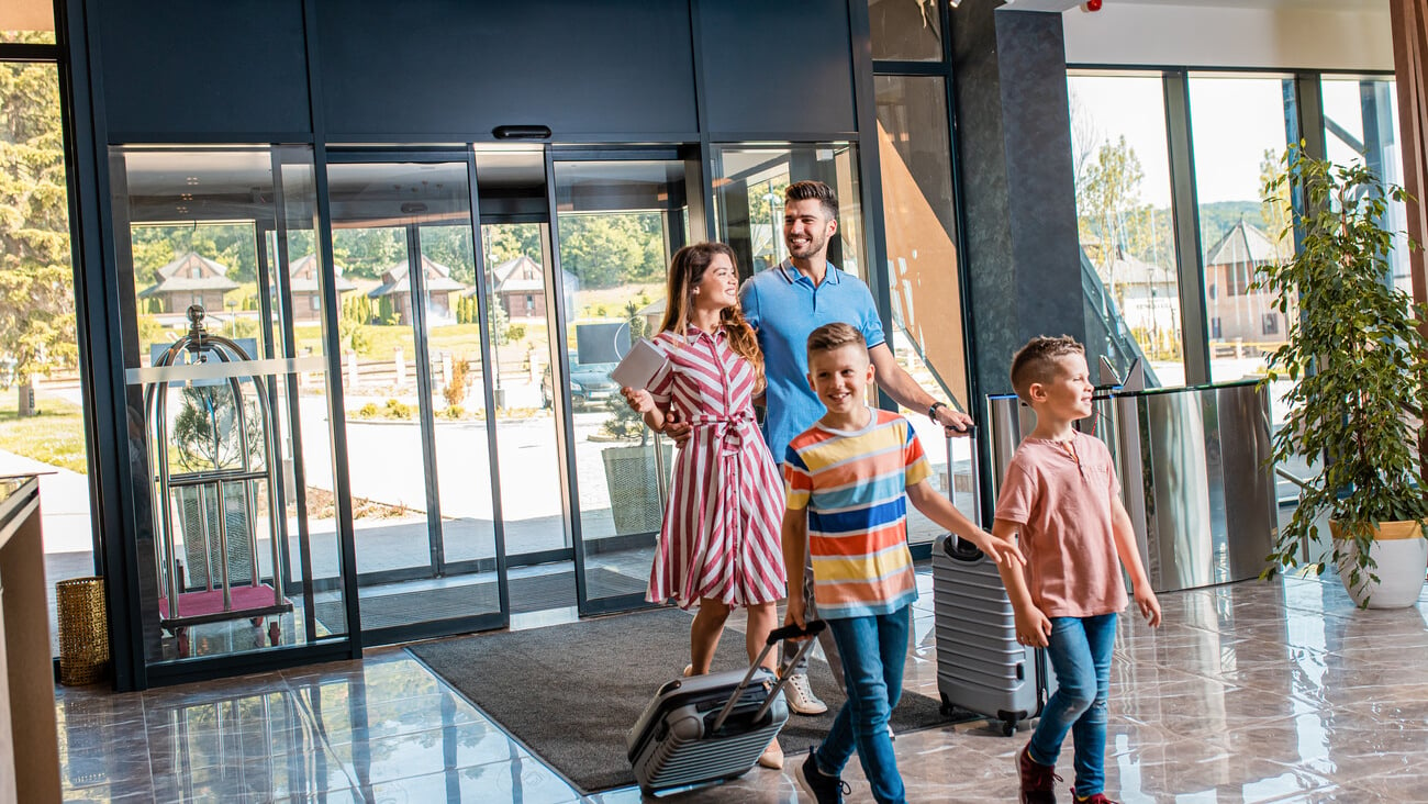 Smiling family of four enters to the hotel lobby to check in at the reception for vacation.; Shutterstock ID 1791376481