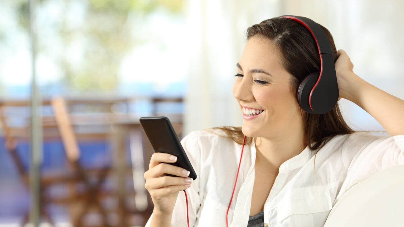 Happy girl listening to music in a beach apartment sitting on a sofa in the living room; Shutterstock ID 758208631