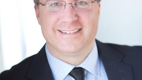 a man wearing a suit and tie smiling at the camera