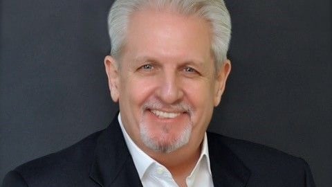 a man wearing a suit and tie smiling at the camera