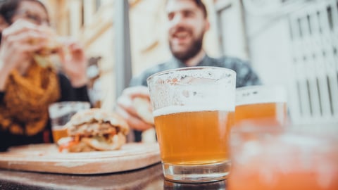 a close up of a glass of beer two people eating outside. 