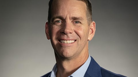 John Padgett wearing a suit and tie smiling at the camera