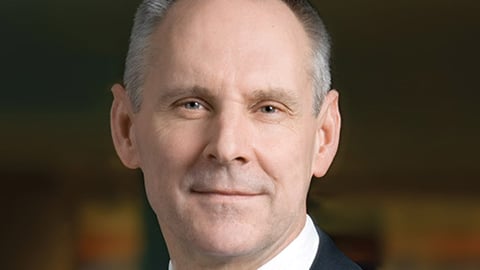 John Davison wearing a suit and tie smiling at the camera