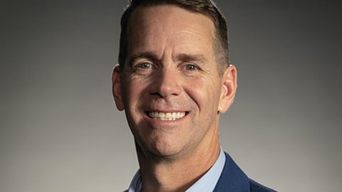 John Padgett wearing a suit and tie smiling at the camera