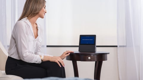 a woman sitting on a bed using an in-room device