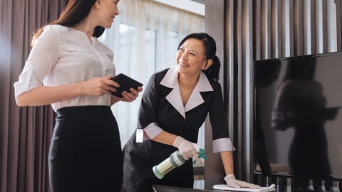 Housekeeping staff using a tablet while cleaning a guestroom