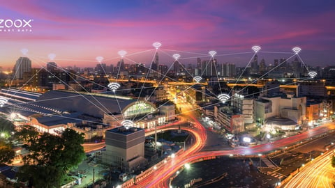 Zoox logo above a city at night displaying internet symbols