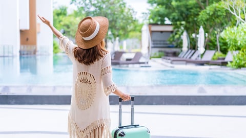 woman standing in front of a hotel pool with suitcase