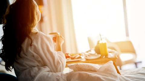 woman watching sunrise from hotel bed with breakfast