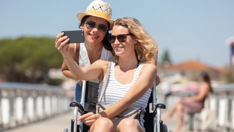 a woman in sunglasses sitting in a wheelchair taking a selfie with a friend