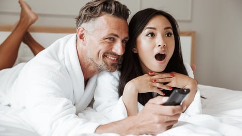 man and woman watching tv in bed