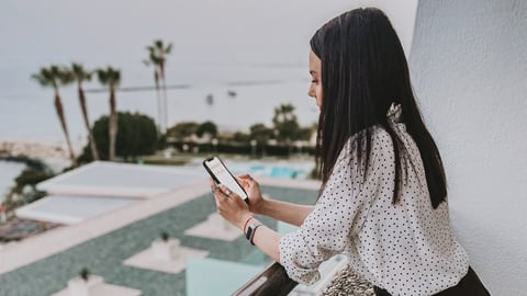 a woman using her smartphone on a hotel balcony overlooking the pool