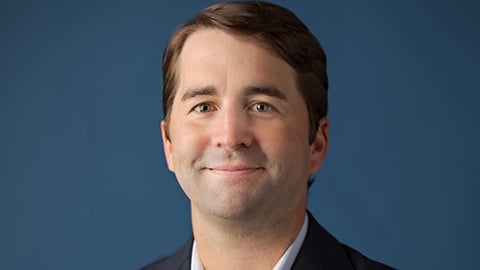 a man wearing a suit and tie smiling and looking at the camera