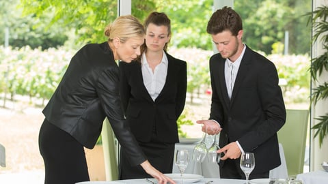 Manager teaches two new hires how to set a table