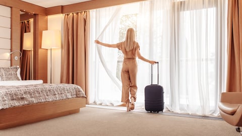 Successful joyful young beautiful well-groomed businesswoman in brown overalls with suitcase settled in luxury room and enjoys magnificent view from window. Young traveler enjoys relaxing in spa hotel; Shutterstock ID 1616234788