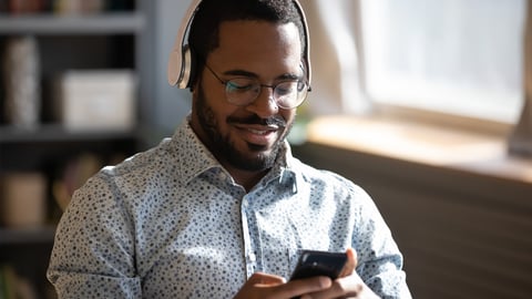 African man wear headphones holds cellphone choose track listens digital music or podcast, using video streaming service. Language learning platform most downloaded education app advertisement concept; Shutterstock ID 1755781163
