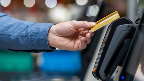 Cropped of adult human's hand placing gold credit card on pos terminal of supermarket during checkout. Anonymous person making contactless transaction and paying for purchases without using cash.; Shutterstock ID 2456593807