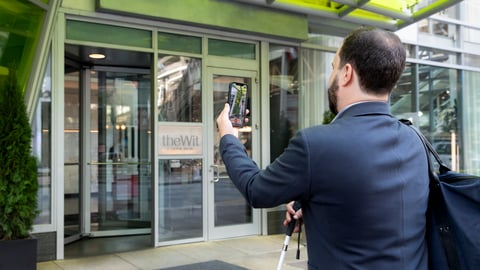 Man using the Be My Eyes app at a Hilton front entrance