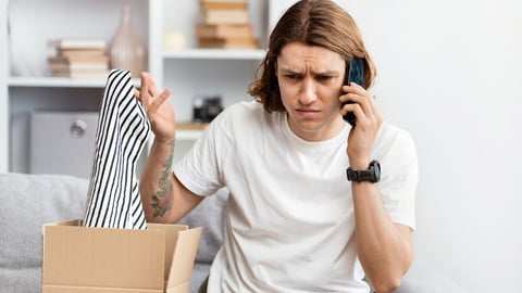 Young Man Unpacking Online Shopping Item, Looks Confused While Talking On Phone, Problem With Order, Suburban Home Background. Indoor, Daylight, Customer Service Issue, Consumer Rights.; Shutterstock ID 2460102123