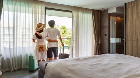 Young couple traveler opening the curtains and looking at the view from the window of a hotel room while on summer vacation, Travel lifestyle concept; Shutterstock ID 2300589961