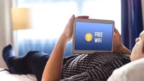 Man using free hotel wifi with tablet. Lying in hotel room bed and browsing internet. Public access online and connection available for customers, visitors and tourists.; Shutterstock ID 1013405500