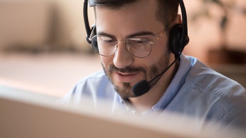 Focused businessman telemarketer telesales agent wear wireless headset make conference video call talk consult online client on computer, male helpline operator work in customer care support office; Shutterstock ID 1443614867