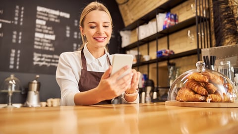 Close up portrait of worker of coffee shop using mobile phone while standing at the wooden table; Shutterstock ID 1840976494