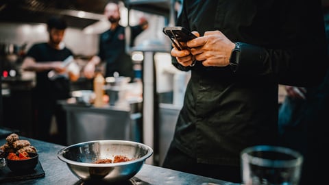 chef with phone in hands on restaurant kitchen; Shutterstock ID 2266863863