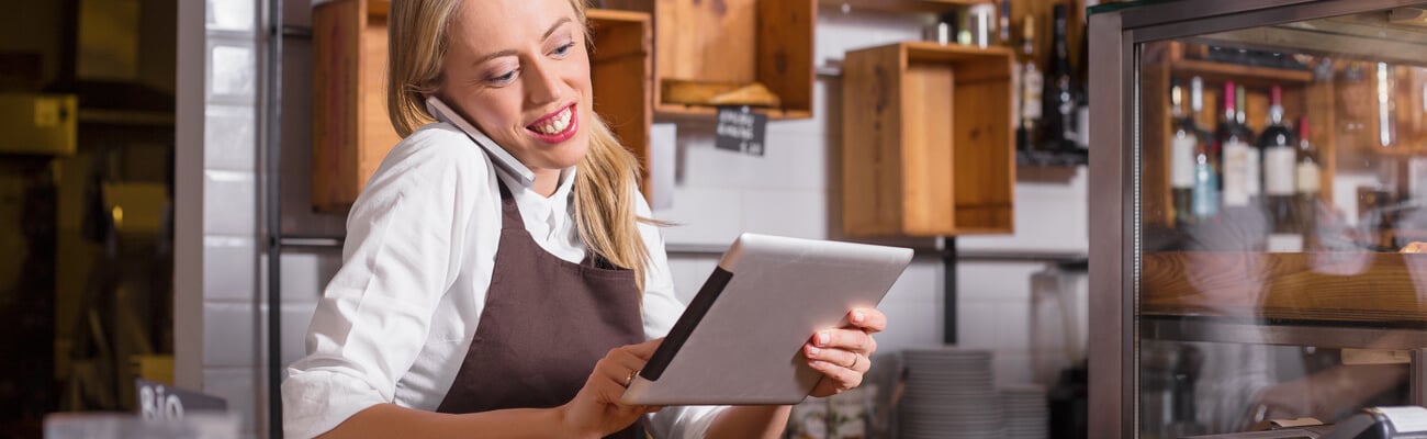 Female barista talking on the phone and using tablet while standing behind the counter; Shutterstock ID 422291380