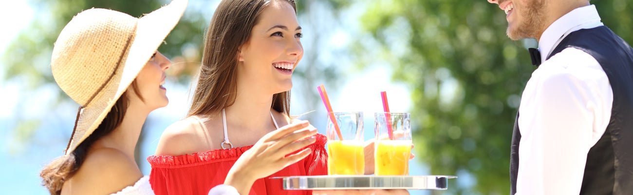 Two hotel customers on summer vacations and a waiter serving them drinks with the ocean in the background; Shutterstock ID 443200663