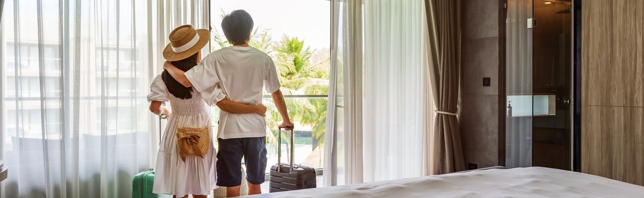 Young couple traveler opening the curtains and looking at the view from the window of a hotel room while on summer vacation, Travel lifestyle concept; Shutterstock ID 2300589961