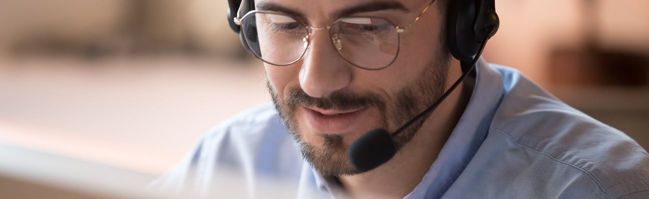 Focused businessman telemarketer telesales agent wear wireless headset make conference video call talk consult online client on computer, male helpline operator work in customer care support office; Shutterstock ID 1443614867