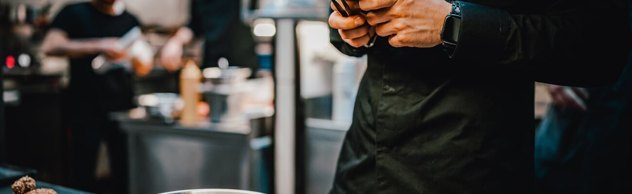 chef with phone in hands on restaurant kitchen; Shutterstock ID 2266863863