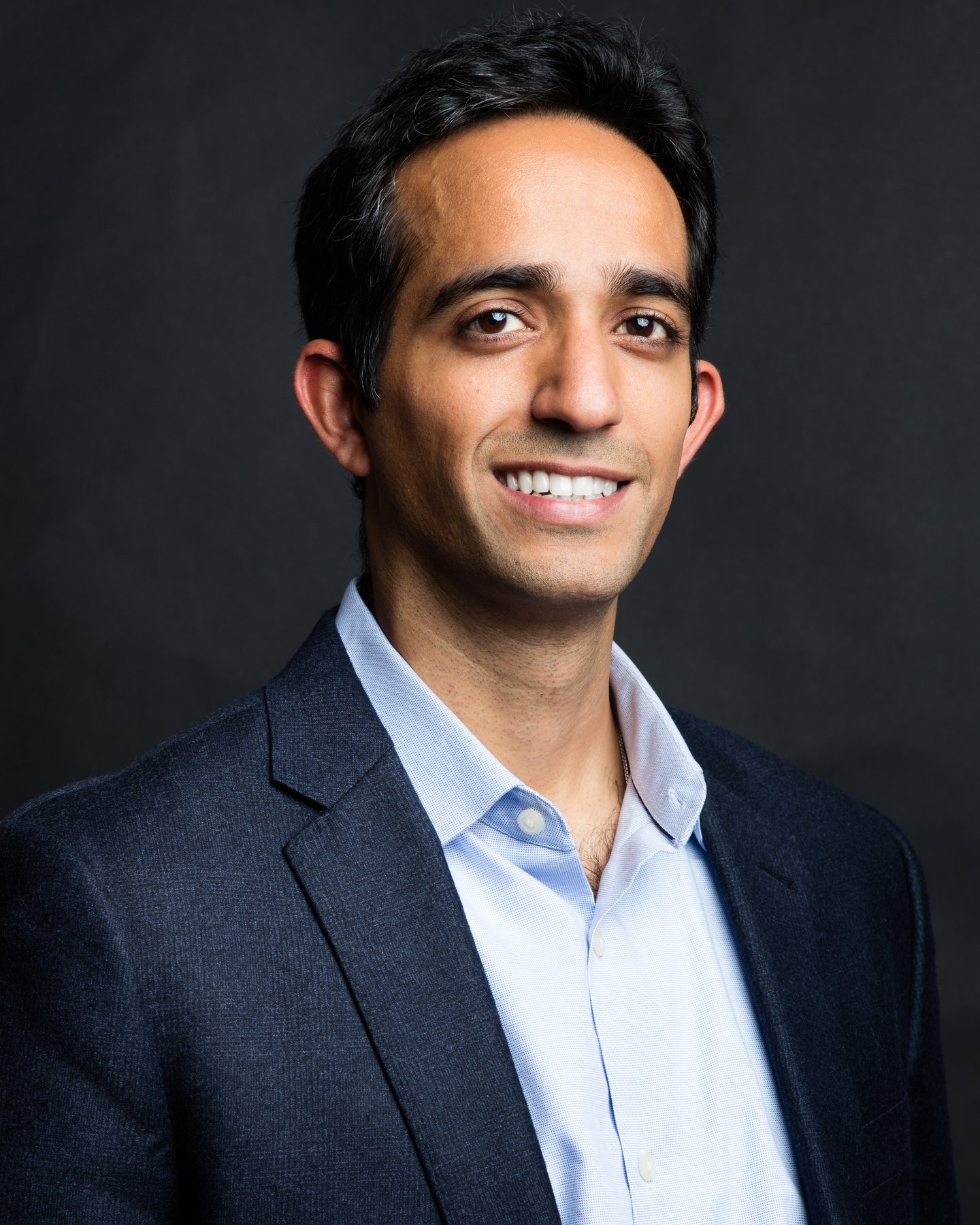 a man wearing a suit and tie smiling and looking at the camera