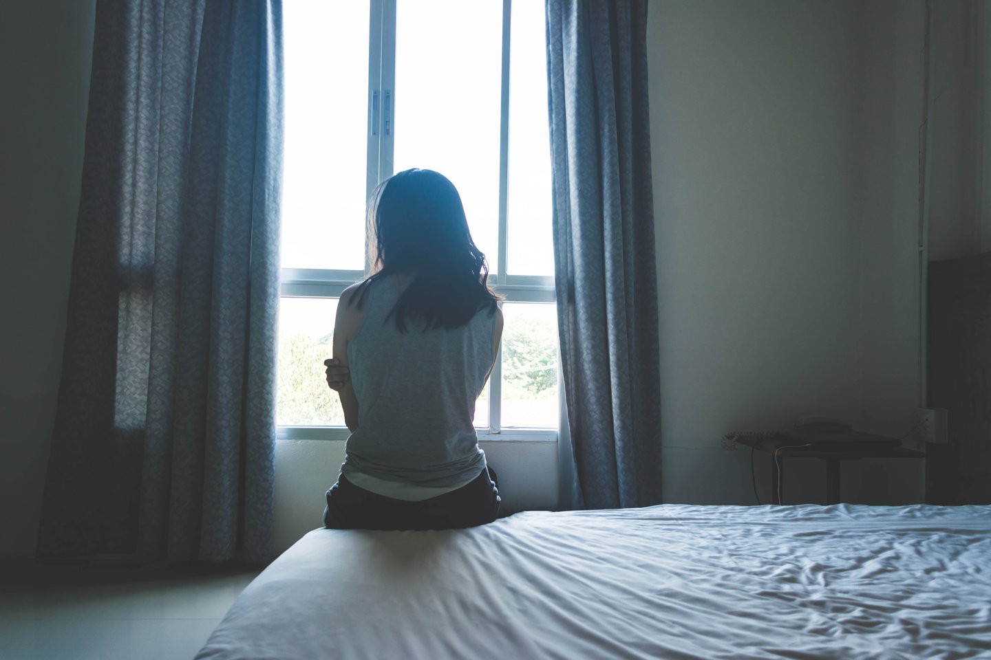 a person sitting on a bed next to a window