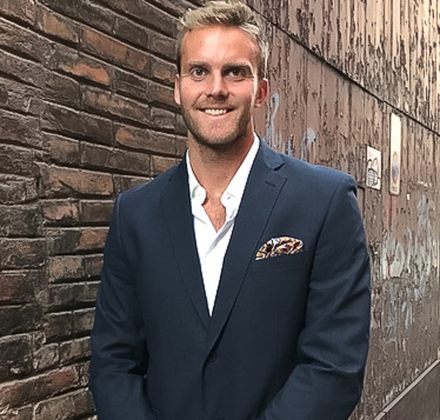 a man wearing a suit and tie standing in front of a brick building