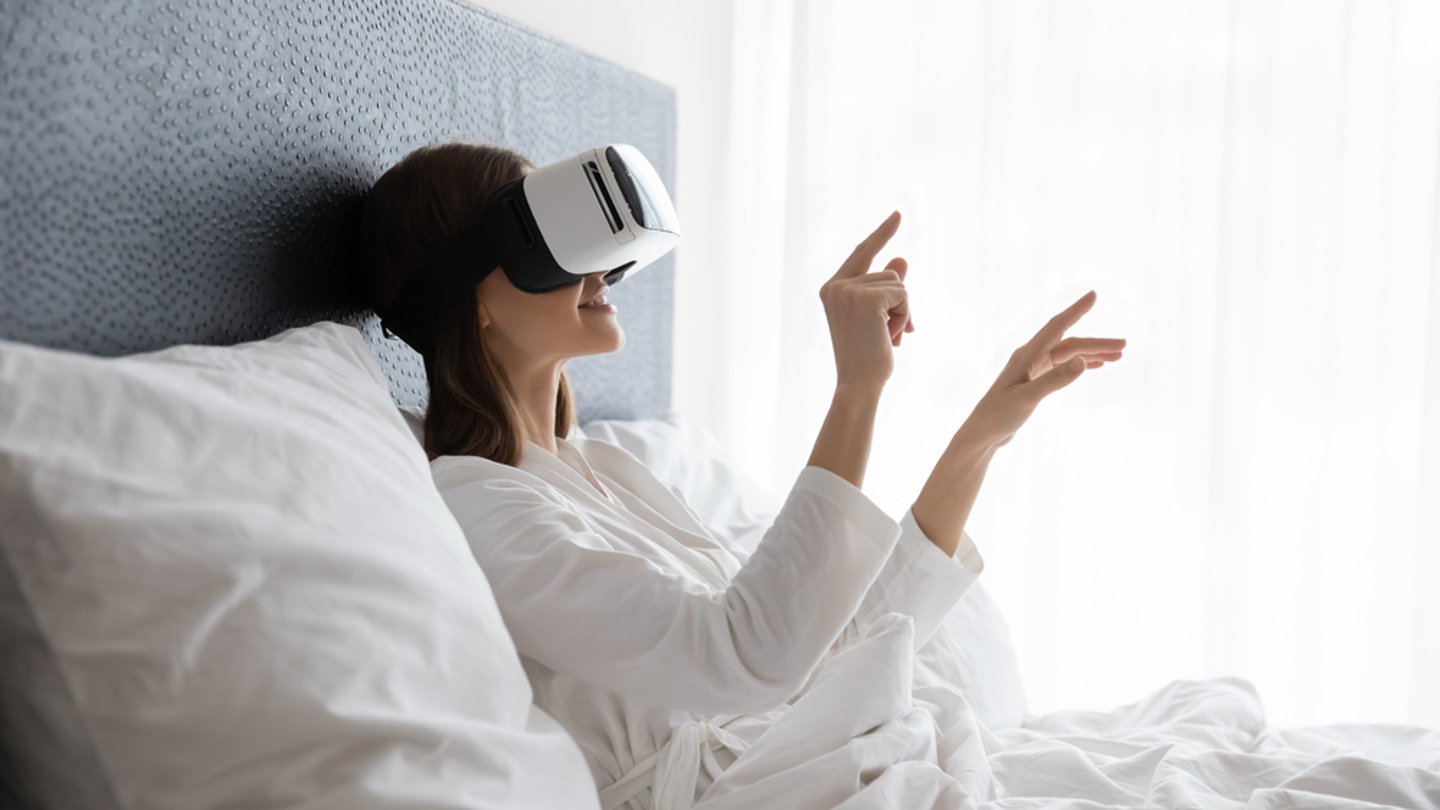 a woman sitting on a hotel bed using a VR headset