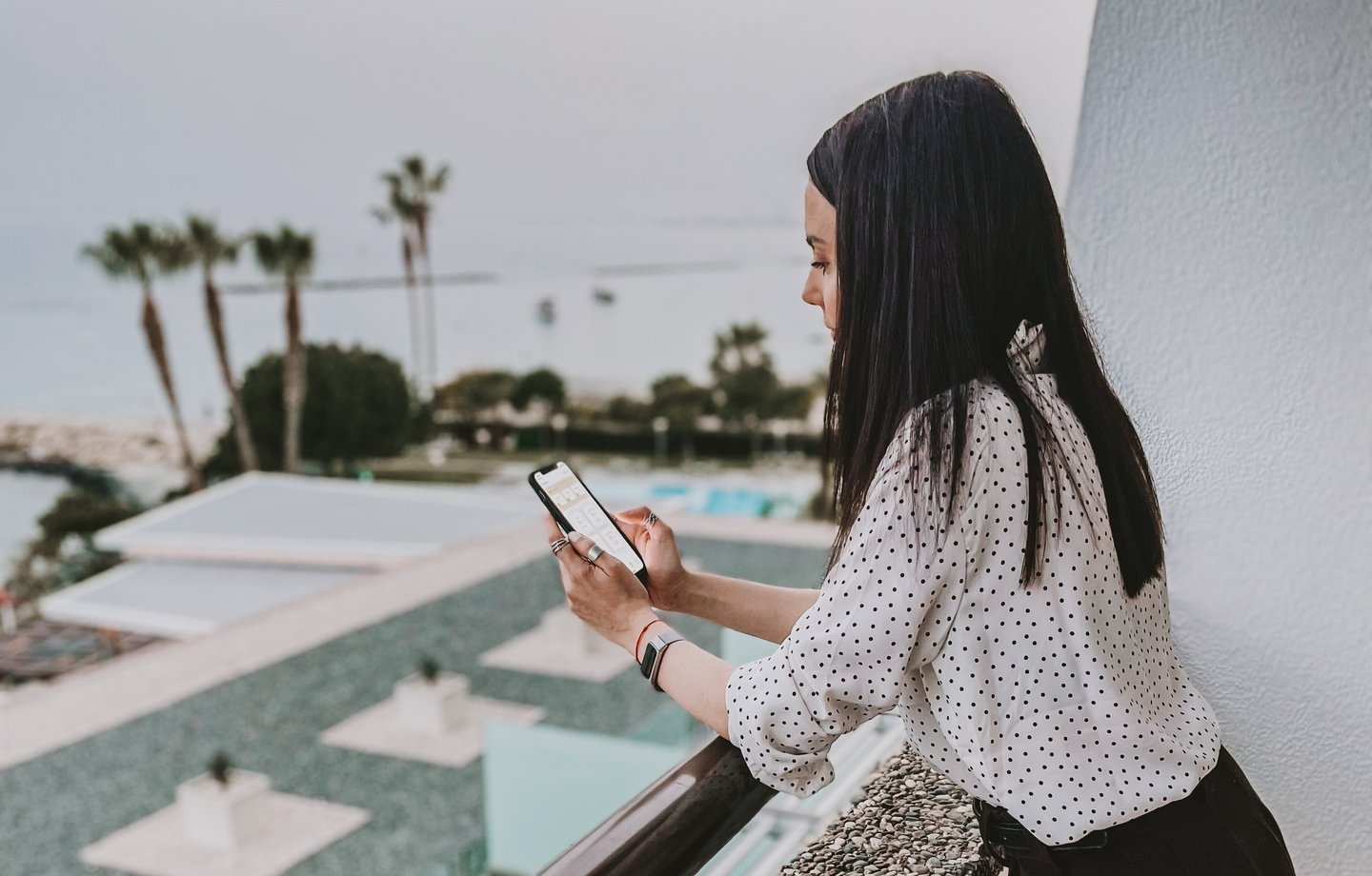 a woman using her smartphone on a hotel balcony overlooking the pool