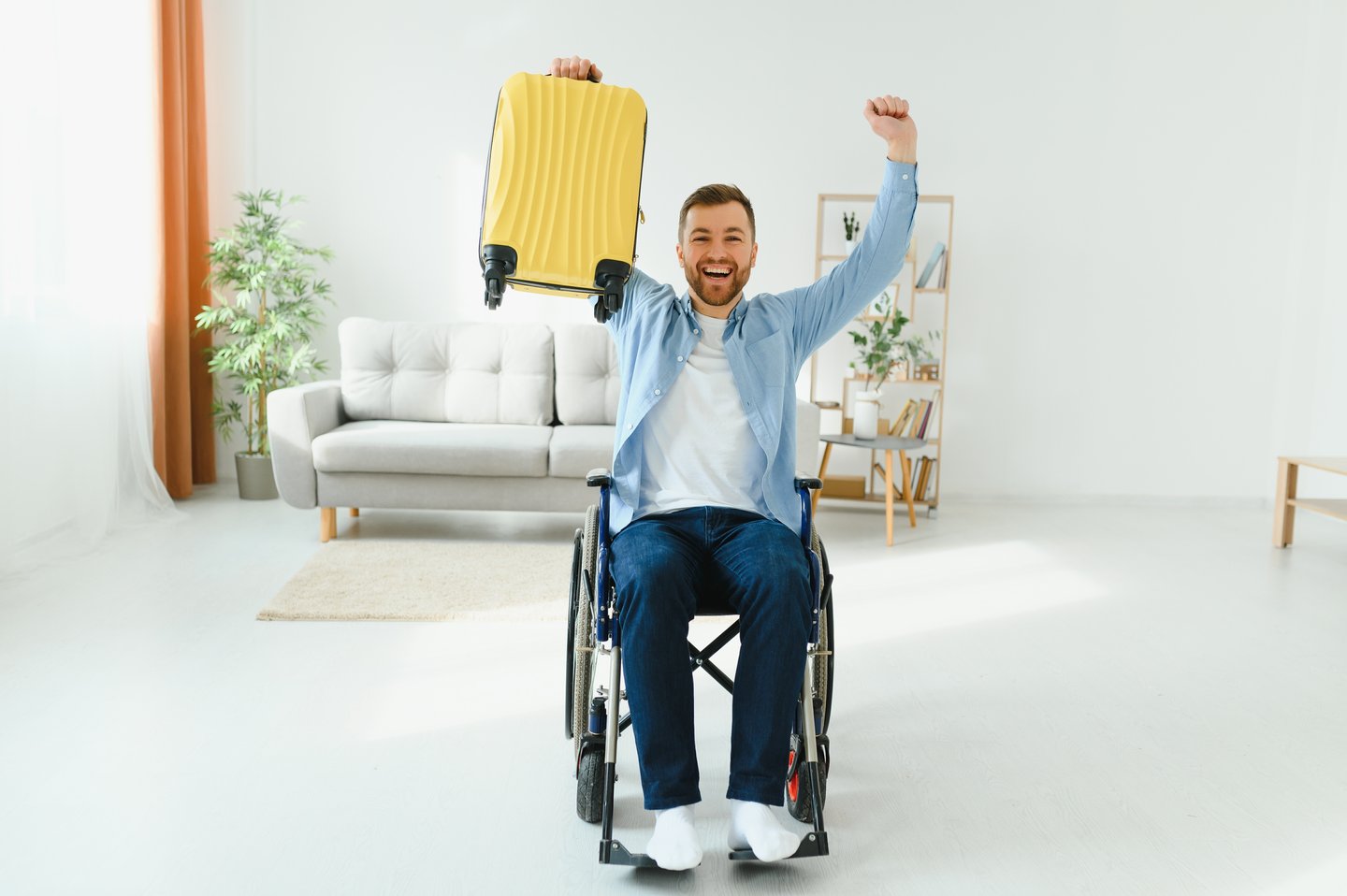 Man in wheelchair holding up yellow suitcase excited for vacation