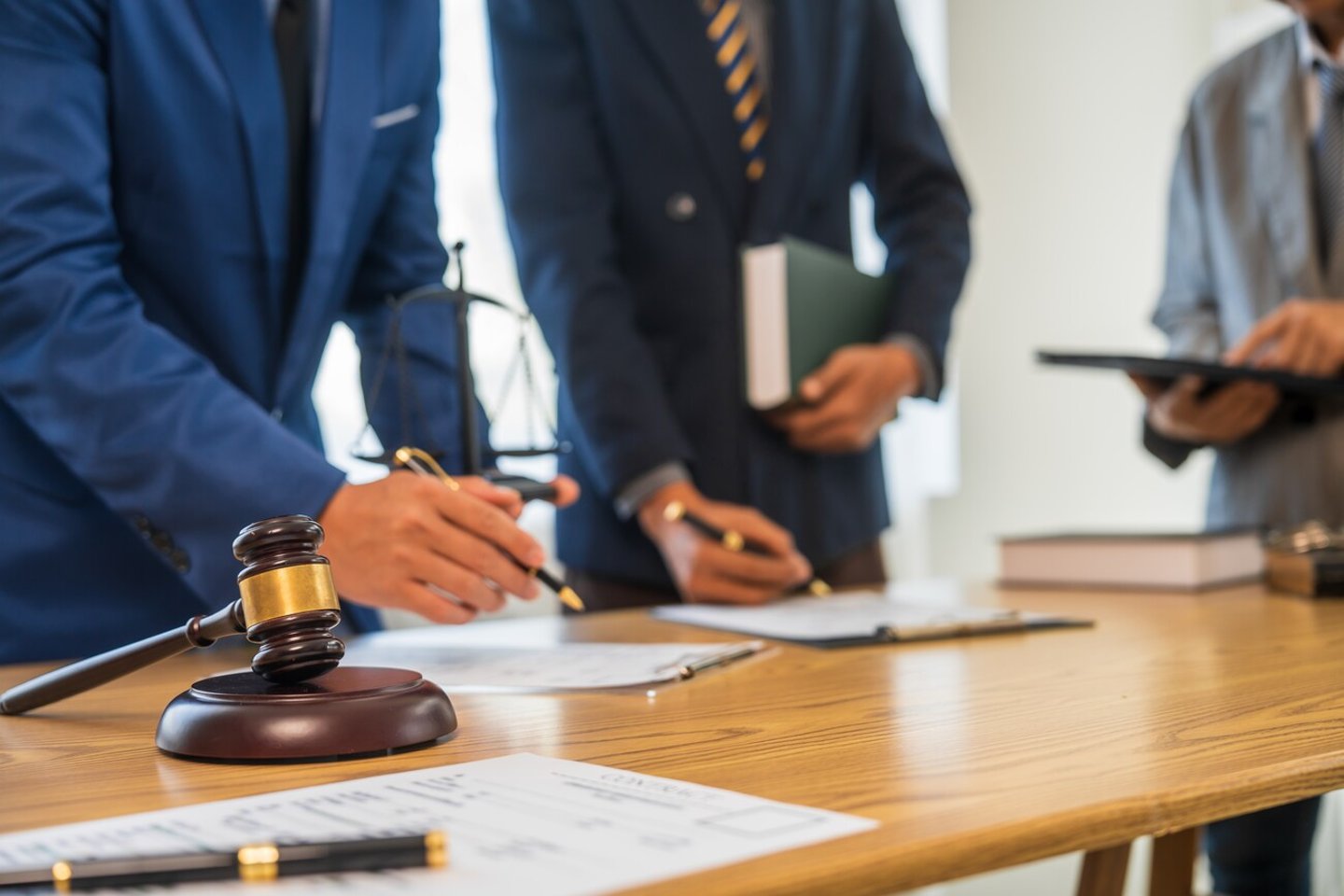 A team meeting of business people and a lawyer in formal suits is taking place at a desk, discussing a contract and various aspects of the law and litigation.; Shutterstock ID 2469307669