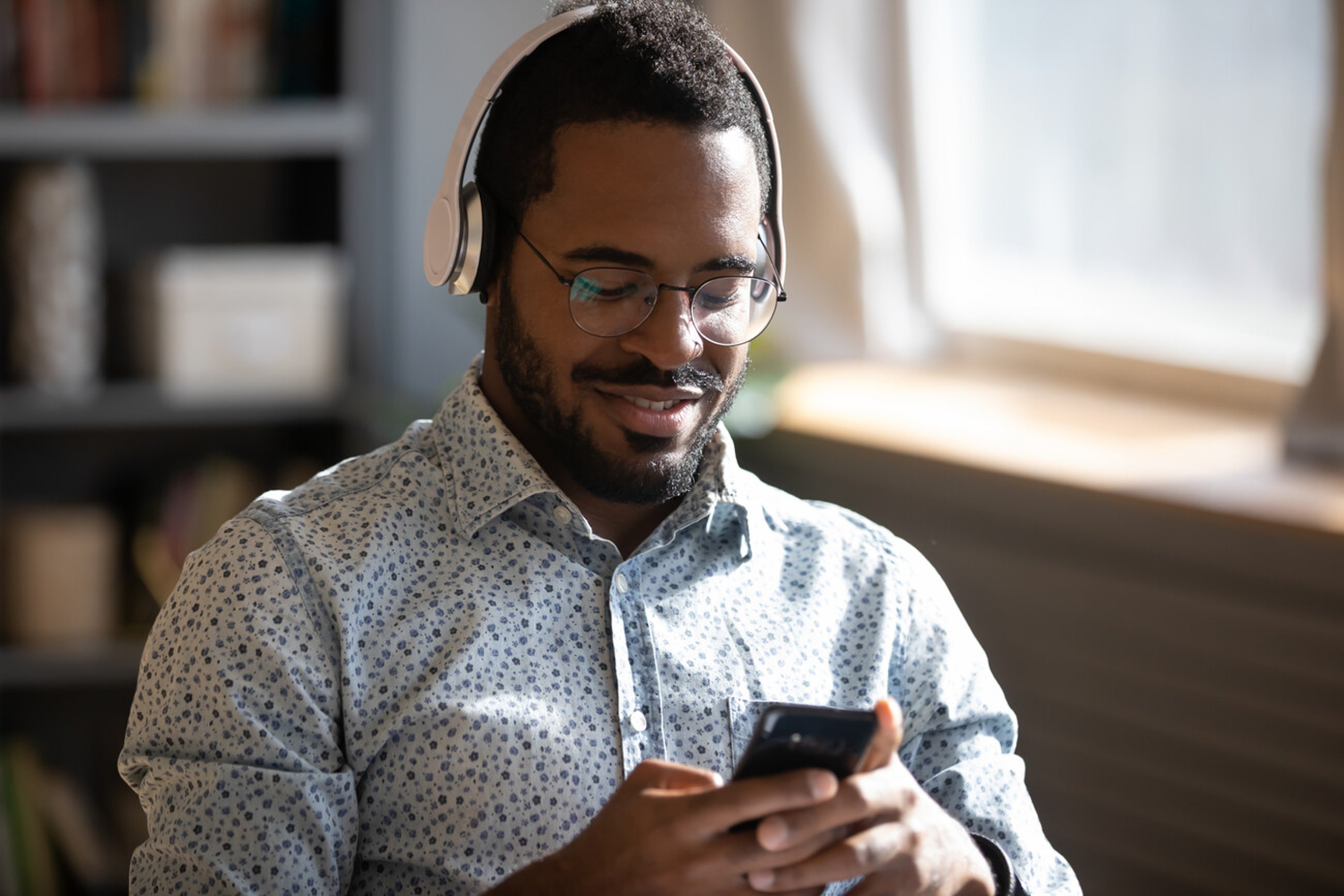 African man wear headphones holds cellphone choose track listens digital music or podcast, using video streaming service. Language learning platform most downloaded education app advertisement concept; Shutterstock ID 1755781163