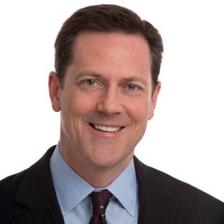 a man wearing a suit and tie smiling at the camera
