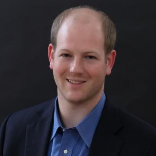 a man wearing a suit and tie smiling at the camera