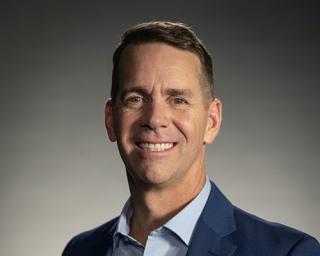 John Padgett wearing a suit and tie smiling at the camera